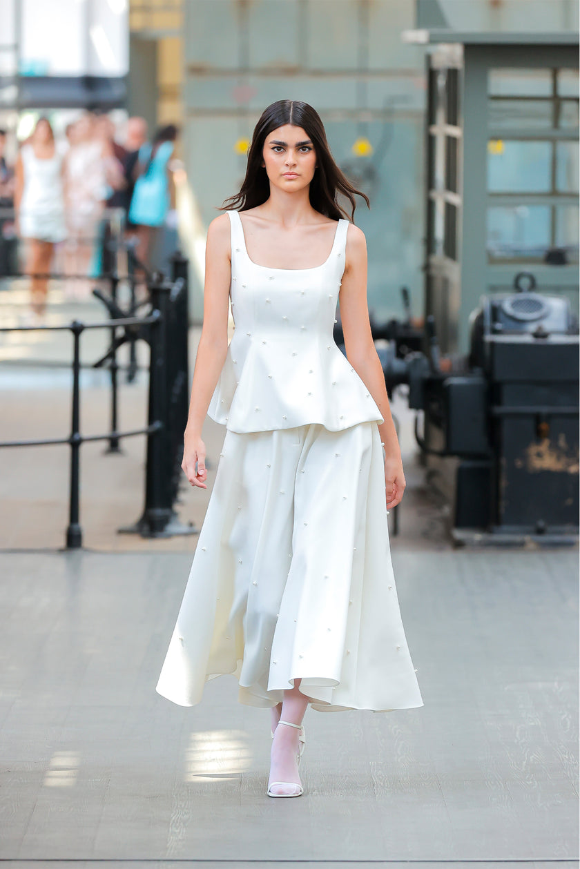 Woman wearing a white dress in an indoor setting with blurred people in the background