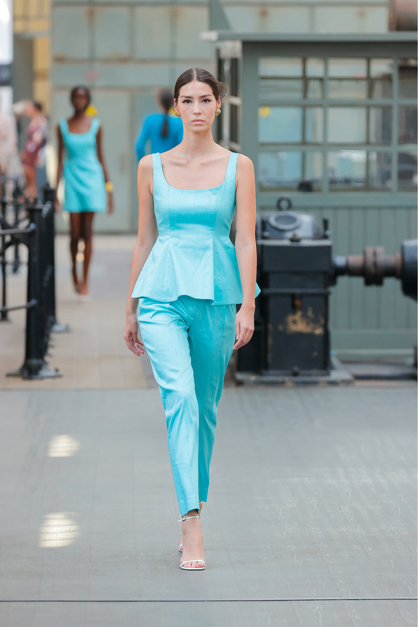 Woman in a turquoise outfit walking on a runway with blurred background