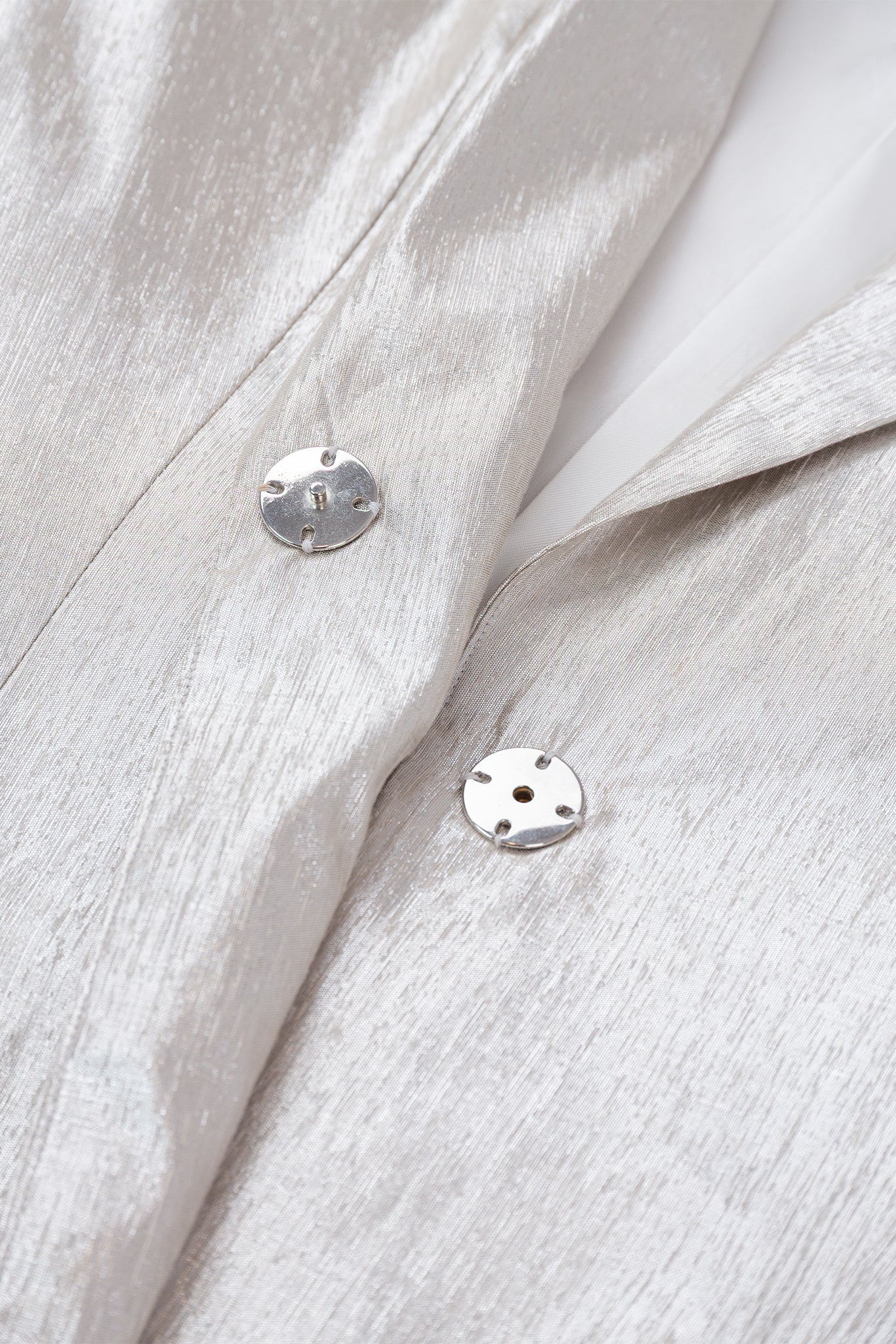 Close-up of a light gray fabric with two silver buttons.