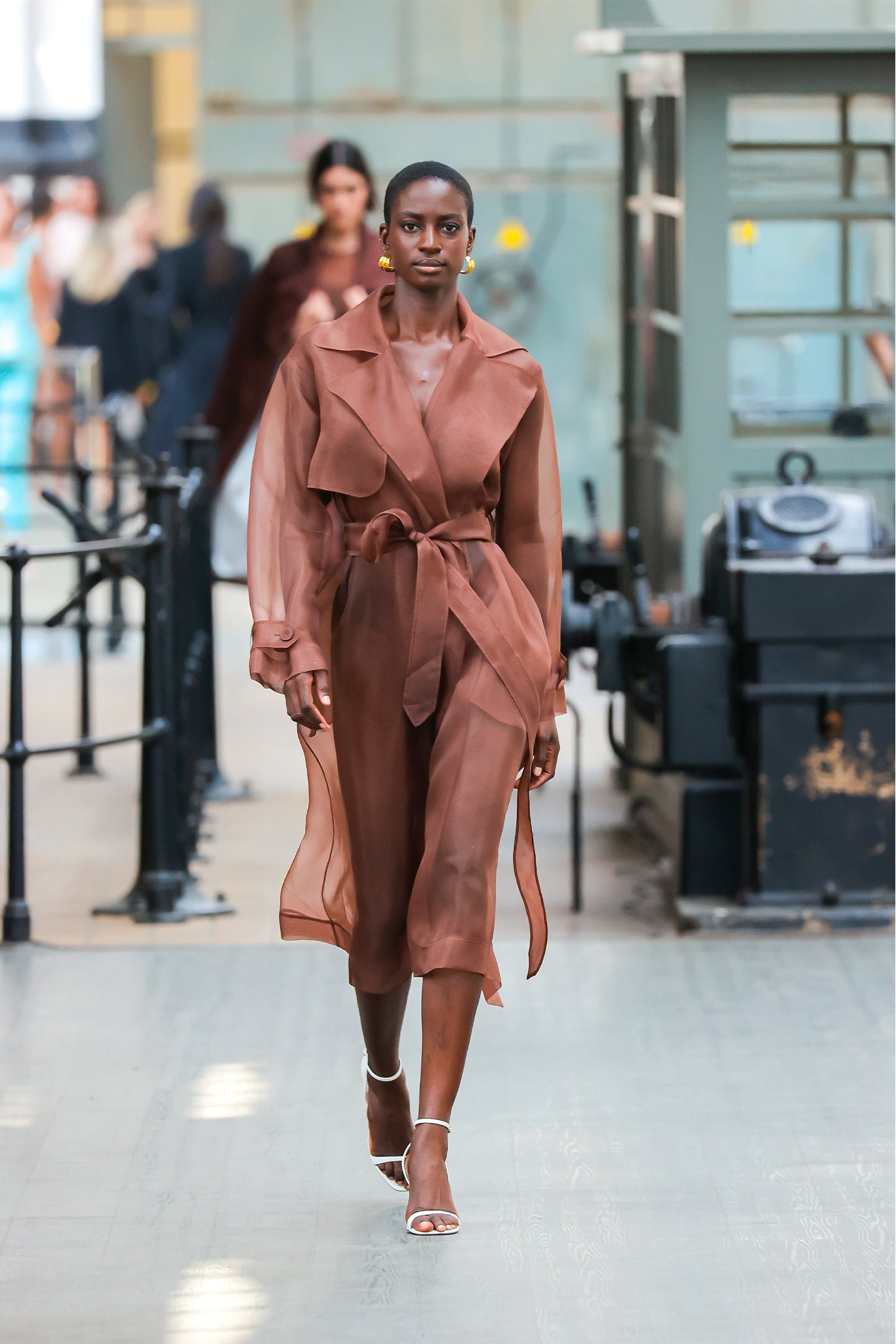 Woman in a brown trench coat walking in an indoor setting
