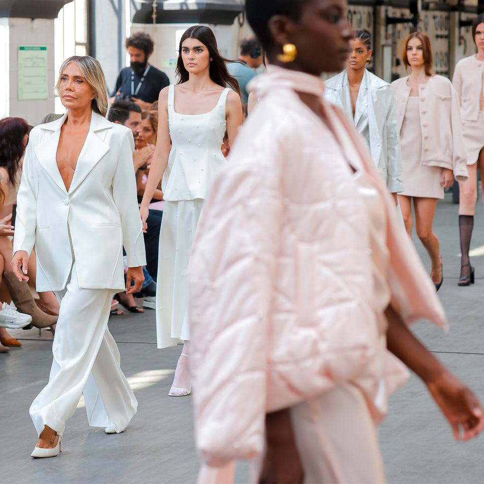 Fashion show with models walking on a runway wearing various outfits.