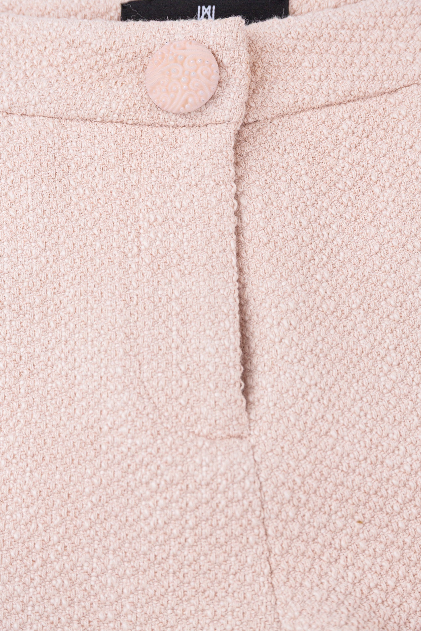 Close-up of a pink textured fabric with a button and brand label.