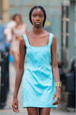 Woman wearing a light blue dress standing outdoors with blurred people in the background