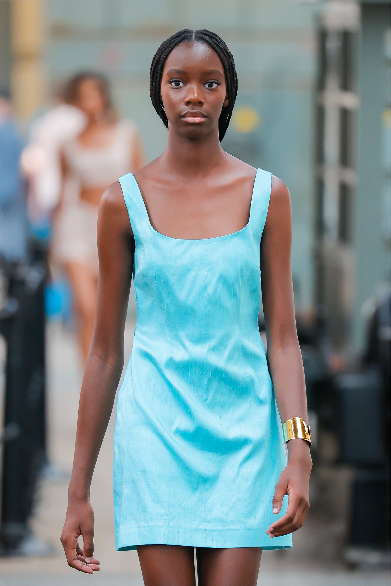 Woman wearing a light blue dress standing outdoors with blurred people in the background