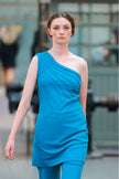 Woman wearing a blue one-shoulder dress in an urban setting