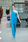 Model wearing a blue outfit walking on a runway with industrial background
