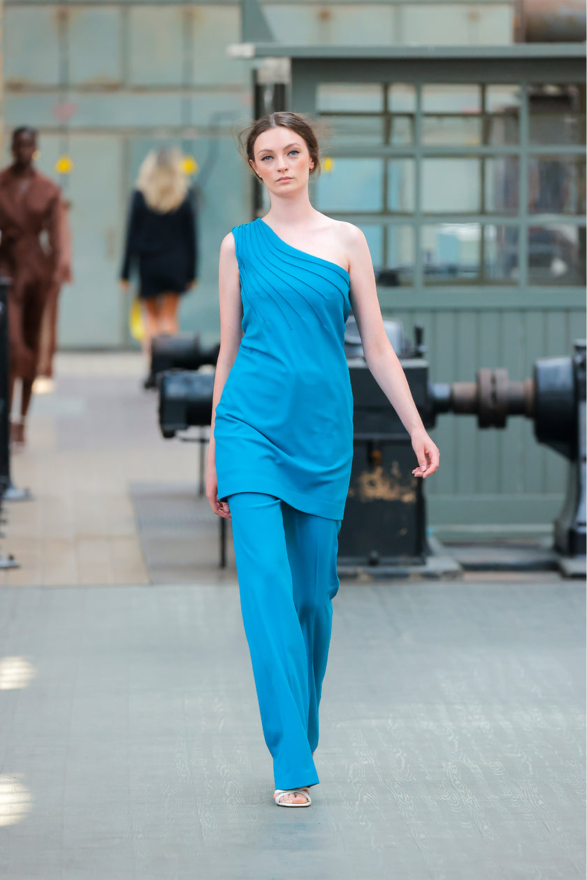 Model wearing a blue outfit walking on a runway with industrial background