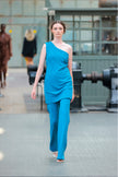 Model wearing a blue one-shoulder dress walking on a runway.