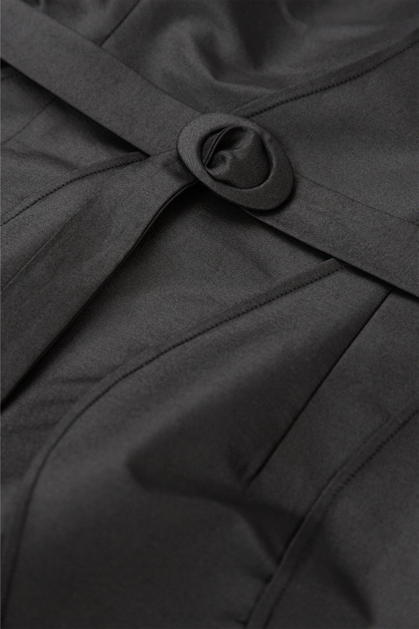 Close-up of a black coat with a belt and button detail.