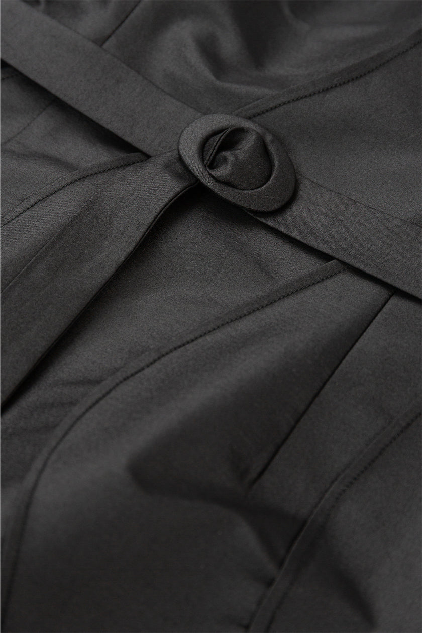 Close-up of a black coat with a belt and button detail.