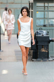 Woman in a white dress walking on a runway with blurred people in the background