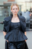 Woman wearing a black peplum top and jacket in an urban setting