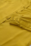 Close-up of a mustard yellow shirt with buttons and a pocket.