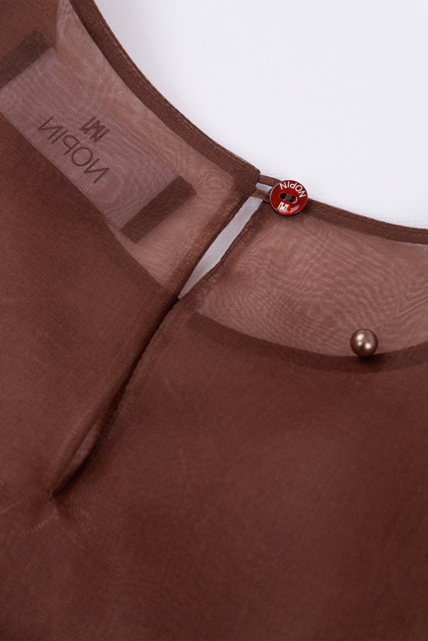 Close-up of a brown garment with a brand label and decorative buttons on a white background