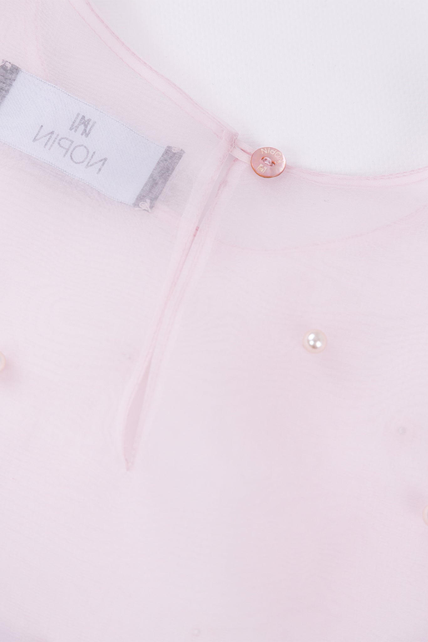 Close-up of a light pink shirt with a button and label detail.