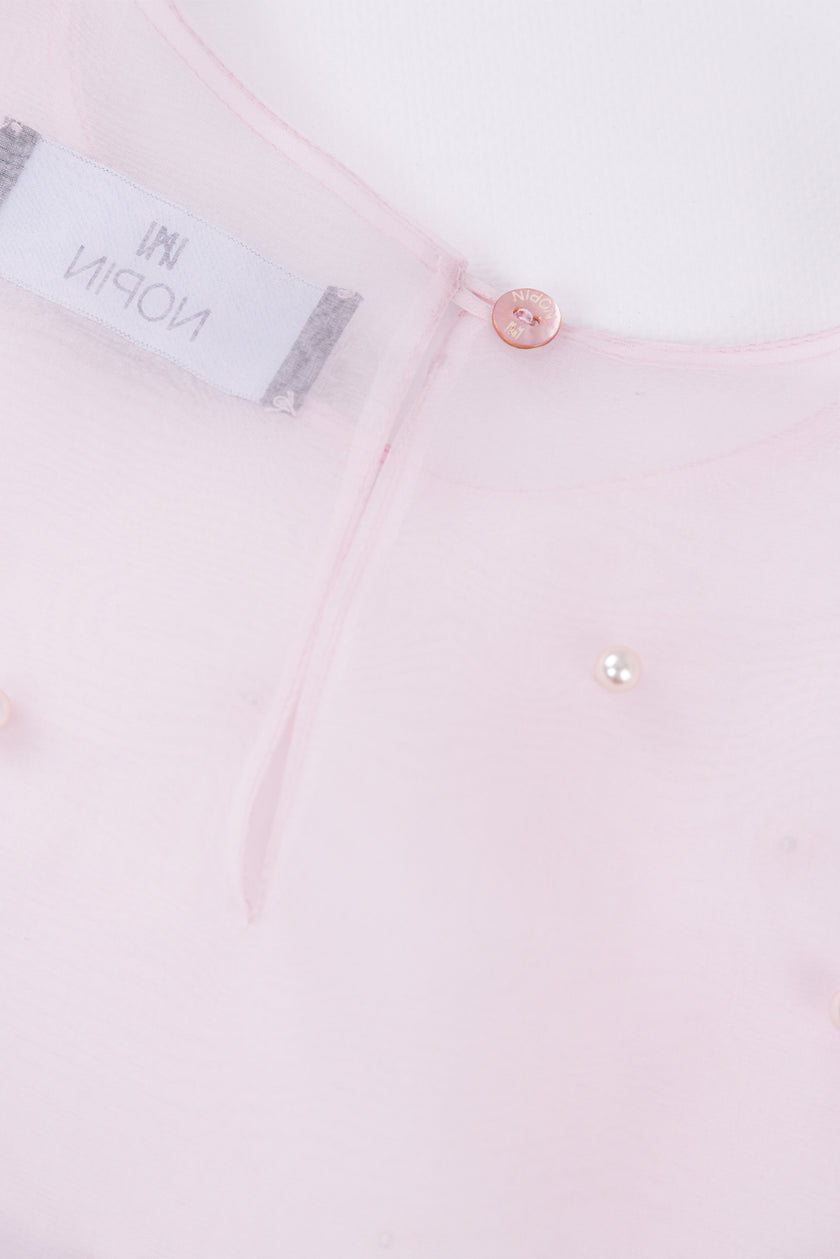 Close-up of a light pink shirt with a button and label detail.