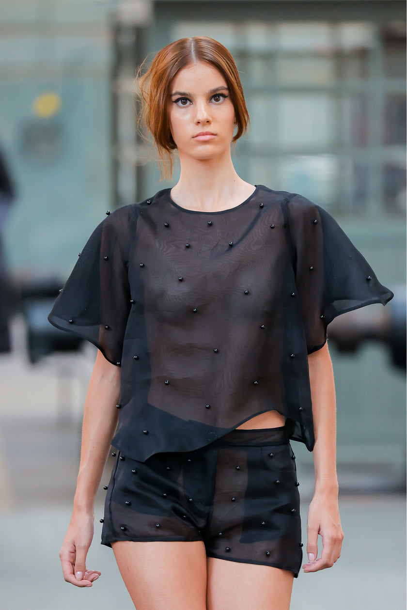 Woman wearing a black outfit with bead details against an urban background