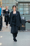 Model wearing a black outfit walking on a runway with a blurred background