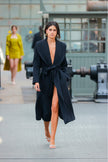 Model wearing a long black coat with a high slit on a runway.