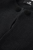 Close-up of a textured black garment with decorative buttons and a visible brand label.