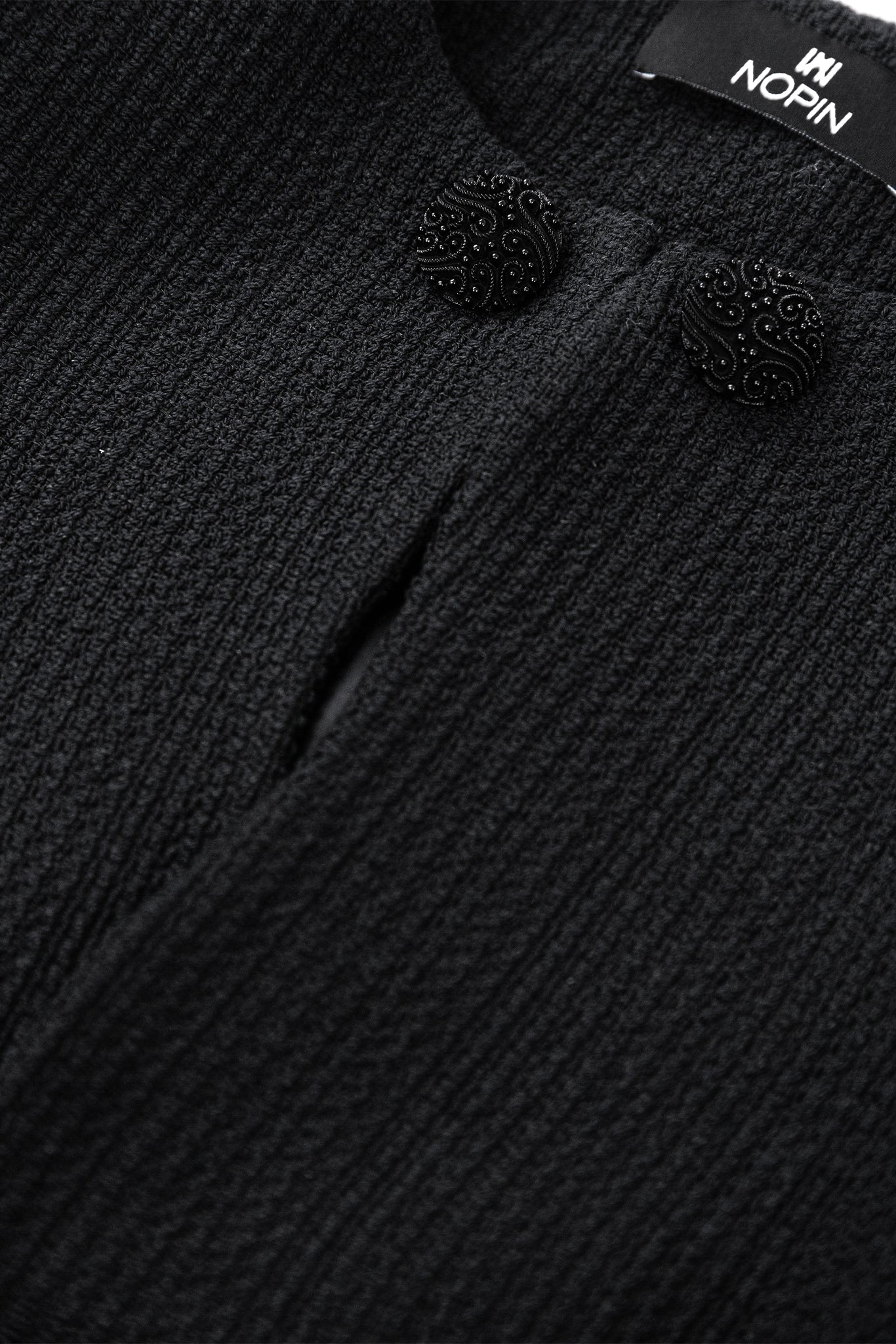 Close-up of a textured black garment with decorative buttons and a visible brand label.