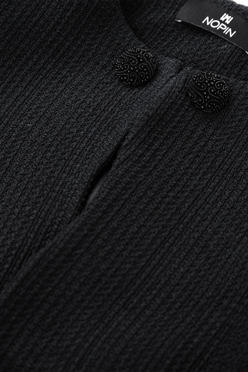 Close-up of a textured black garment with decorative buttons and a visible brand label.