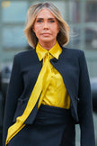 Woman wearing a black blazer and yellow shirt with a blurred background