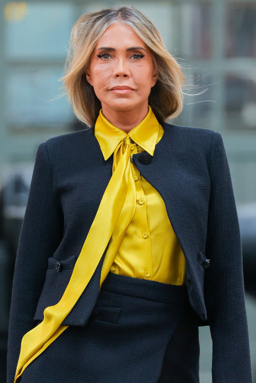 Woman wearing a black blazer and yellow shirt with a blurred background