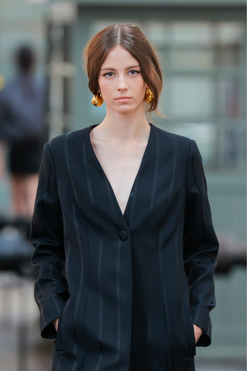 Woman wearing a black blazer over a beige top with a blurred background