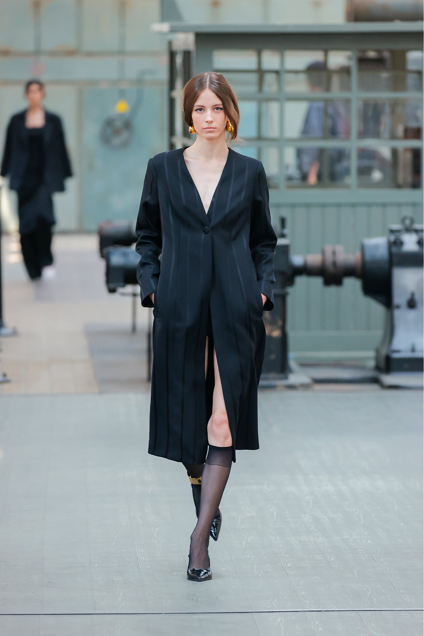 Woman in a black dress walking on a runway with an industrial background
