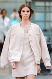 Woman wearing a light pink outfit with a jacket and dress on a blurred background