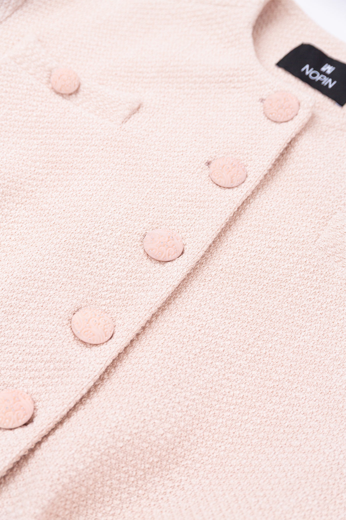 Close-up of a pink textured fabric with buttons and a brand label.