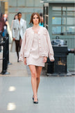 Woman in a light pink outfit walking on a runway.
