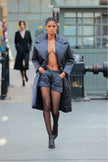 Model wearing a long black puffer coat over a black outfit with high heels on a city street.